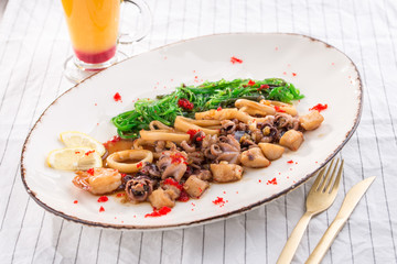 Seafood platter with squid, octopus and scallop and orange drink on white fabric background