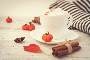 Spicy pumpkin latte, autumn hot drink white cup, with pumpkins, cinnamon and spices on old rustic wooden background copy space