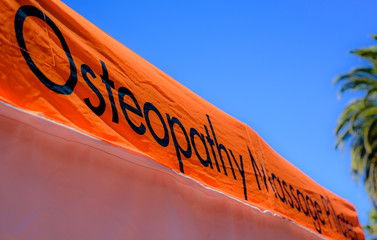 Osteopathy sign on bright orange background against blue sky with copy space, selective focus