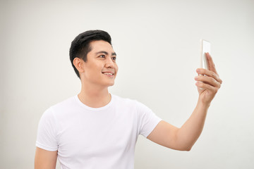 Smiling young asian man making selfie photo on smartphone over white background