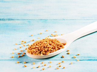 Fenugreek (Trigonella) in a wooden spoon on a blue, wooden background diagonally