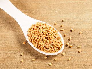 Fenugreek (Trigonella) in wooden spoon on a wooden background diagonally. Macro