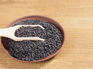 Black sesame (Sesamum indicum) in a clay plate with scoop on a wooden background