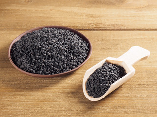 Black sesame (Sesamum indicum) in a clay plate with white scoop on a wooden background