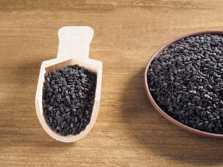Black sesame (Sesamum indicum) in a clay plate with white scoop on a wooden background