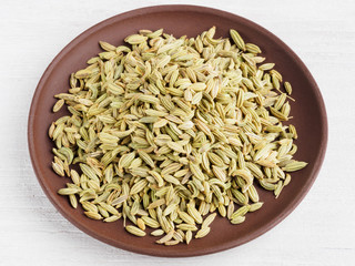 Fennel seeds (Foeniculum vulgare) in a brown clay plate on a white background