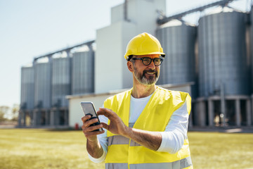 worker using smartphone standing in front of grain silos