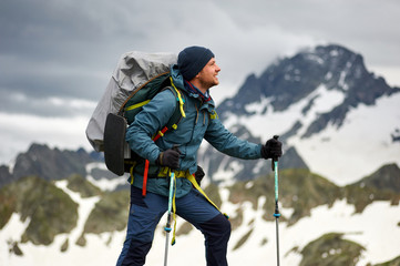 Hiker man stands on the cliff against the top of a mountain. Man has a backpack and trekking poles. Mountain trekking. Copy space