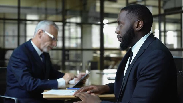 Mature business man refusing african job candidate reading resume on tablet