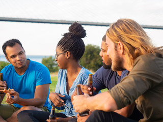 Side view of smiling friends having picnic in park. Cheerful young guys sitting on green grass and eating pizza. Concept of picnic