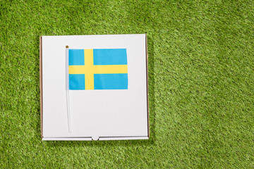 Paper box of pizza with Swedish Flag on the grass. Concept. Top view