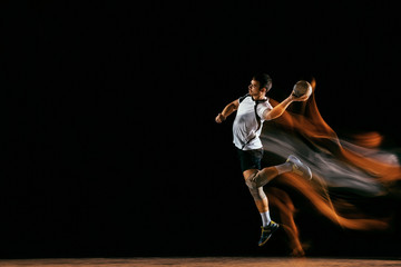Caucasian young handball player in action and motion in mixed lights over black studio background. Fit male professional sportsman. Concept of sport, movement, energy, dynamic, healthy lifestyle. - obrazy, fototapety, plakaty