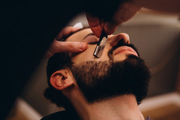 Hair beard and mustache treatment in barber shop. Young, bearded, muscular,  handsome barber making...
