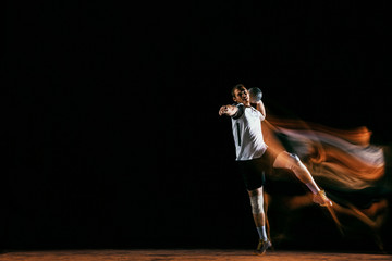Caucasian young handball player in action and motion in mixed lights over black studio background....