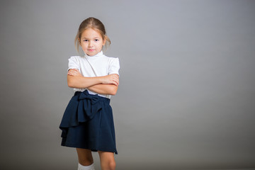 The girl the first grader in a school uniform - a skirt and a white blouse poses on a gray background