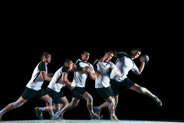 Obraz premium Caucasian young handball player in action and motion in mixed and strobe light on black studio background. Fit professional sportsman. Concept of sport, movement, energy, dynamic, healthy lifestyle.