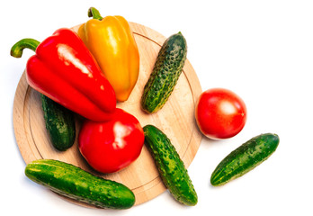cucumbers, peppers and tomatoes on a wooden cutting board on a white background. vegetables on a round cutting board