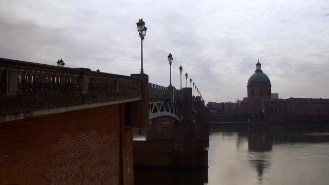 This shot captures an urban bridge Saint Pierre in Toulouse, France. The handrails and lamp posts, combined with a silver sky, paint a scenic picture.