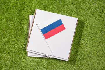 Paper box of pizza with Russian Flag on the grass. Concept. Top view