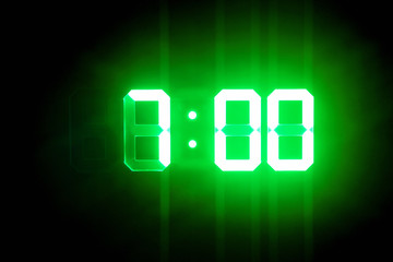 Green glowing digital clocks in the dark show 7:00 time