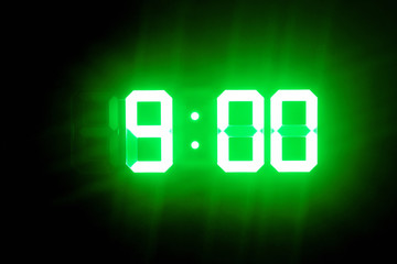 Green glowing digital clocks in the dark show 9:00 time