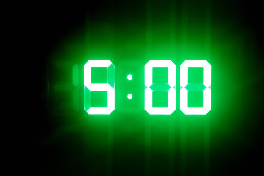 Green glowing digital clocks in the dark show 5:00 time