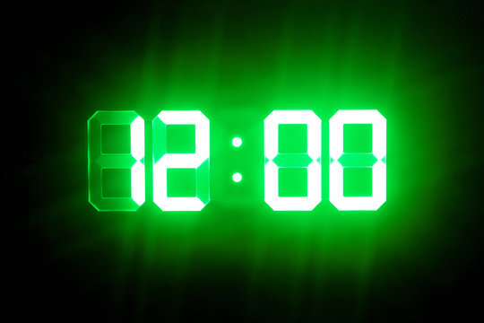 Green glowing digital clocks in the dark show 12:00 time