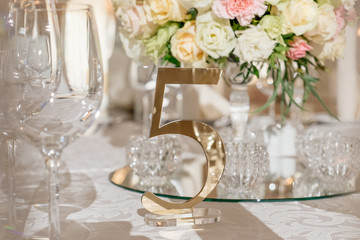 Golden number five on a decorated table for a wedding dinner. Festive banquet table setting. White, light pink wedding decor with fresh flowers.