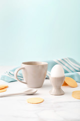 Fototapeta na wymiar Boiled egg in ceramic egg cup, cup of coffee and thin crispy corn chips on background of turquoise kitchen towel. Breakfast concept.
