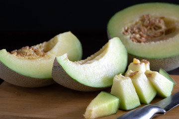 Fresh melon fruit cut to piece on chopping wood and dark table