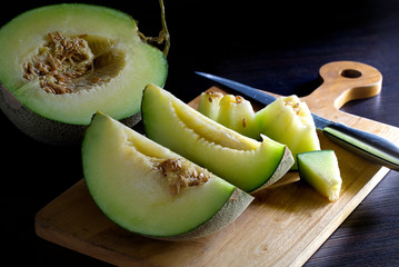 Fresh melon fruit cut to piece on chopping wood and dark table