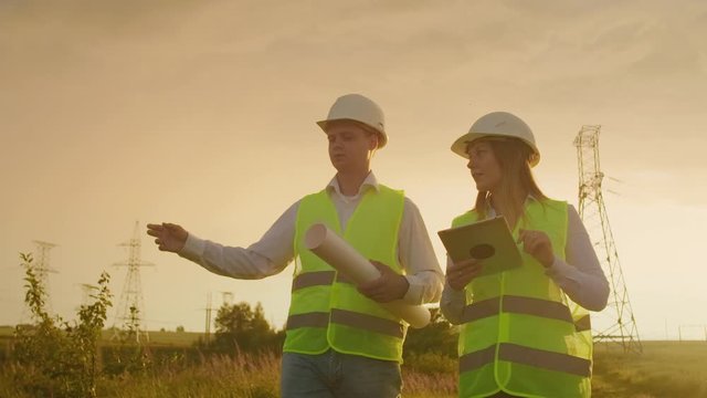 Coworking engineers with tablets on solar plant. Adult men and women in hardhats using tablets while standing outdoors on transformer platform. Transportation of clean energy