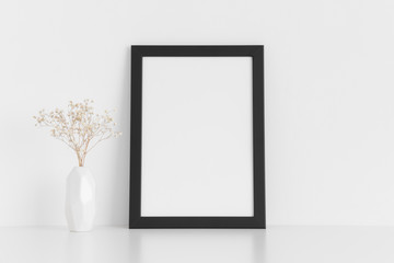 Black frame mockup with a gypsophila in a vase on a white table.Portrait orientation.