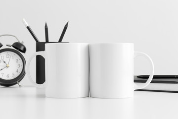 Two white mugs mockup with workspace accessories on a white table.