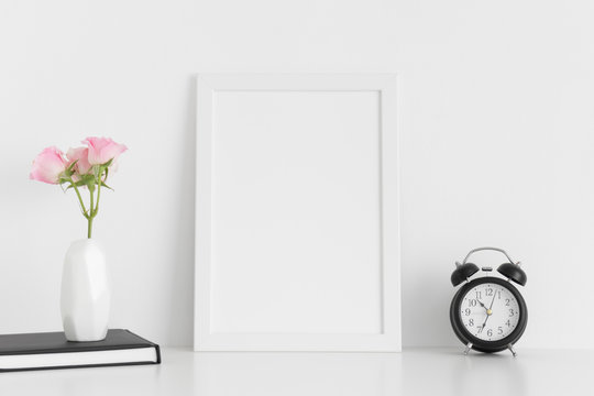 White frame mockup with workspace accessories  and pink roses in a vase on a white table.Portrait orientation.