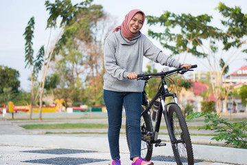 portrait of hijab woman posing next to a bicycle and pushing her bicycle in front of the camera