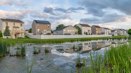 Fototapeta na wymiar Panorama Beautiful multi storey homes built in front of a grassy and shiny pond