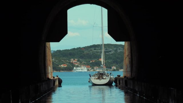 Beautiful shoot from the inside of the submarine/military tunnel. A sailboat is parked outside on a summer day while a ferry ship is passing by. Travel holiday destination. 
