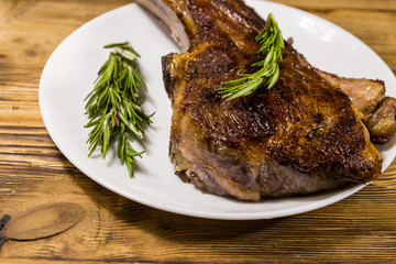Roasted beef rib eye steak on bone with rosemary in white plate on wooden table