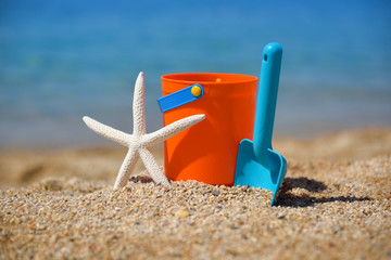 Bright plastic сhildren's beach toys and a starfish on sand near sea. Summer vacation concept