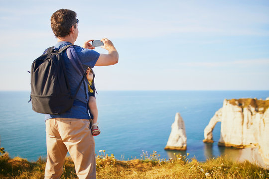 Man carrying his baby in baby carrier and taking a photo of panoramic landscape in Etretat