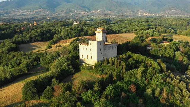 Aerial view of beautiful stone fortress in medieval style on high hill among green trees and bushes in picturesque place on sunny summer evening. Concept of unique architectural medieval structures