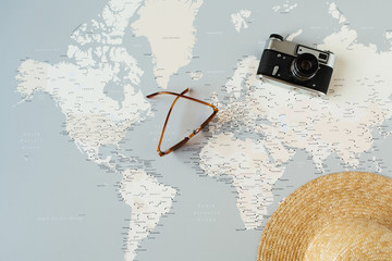 Minimal world map with pins, retro camera, sunglasses, straw hat. Flat lay vacation traveling...