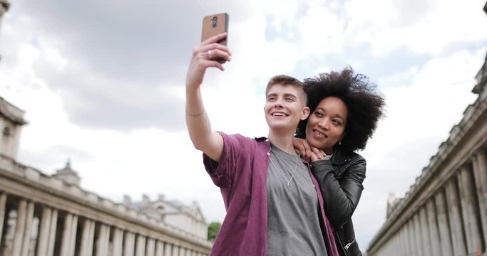 Young adult lesbian couple taking photos of tourist landmark on smartphone