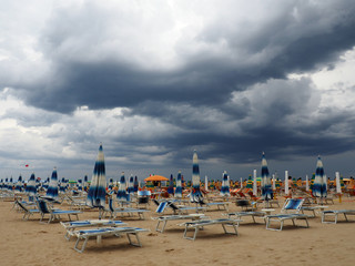 Fototapeta na wymiar Sea, beach and closed sunshades approaching thunderstorms