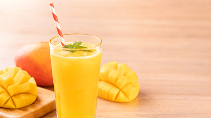 Fresh mango juice with beautiful chopped pulp flesh and straw on bright wooden table background....