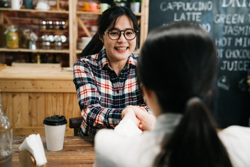 Young asian woman in business employment interview shaking hands with personnel officer in coffee store. smiling girl job seeker handshaking with lady hr manager joyful being hired in cafe bar.