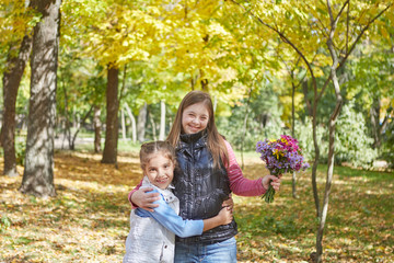 Girl with Down syndrome and little girl in autumn park.