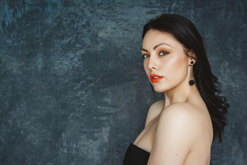 Fototapeta premium Fashionable portrait beautiful woman of a stylish brunette with red lips. Woman with long hair wearing black earrings. Set on gray background