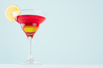 Bright summer beverage margarita for party with red and yellow liquor, orange slice on white wood board and mint color wall.